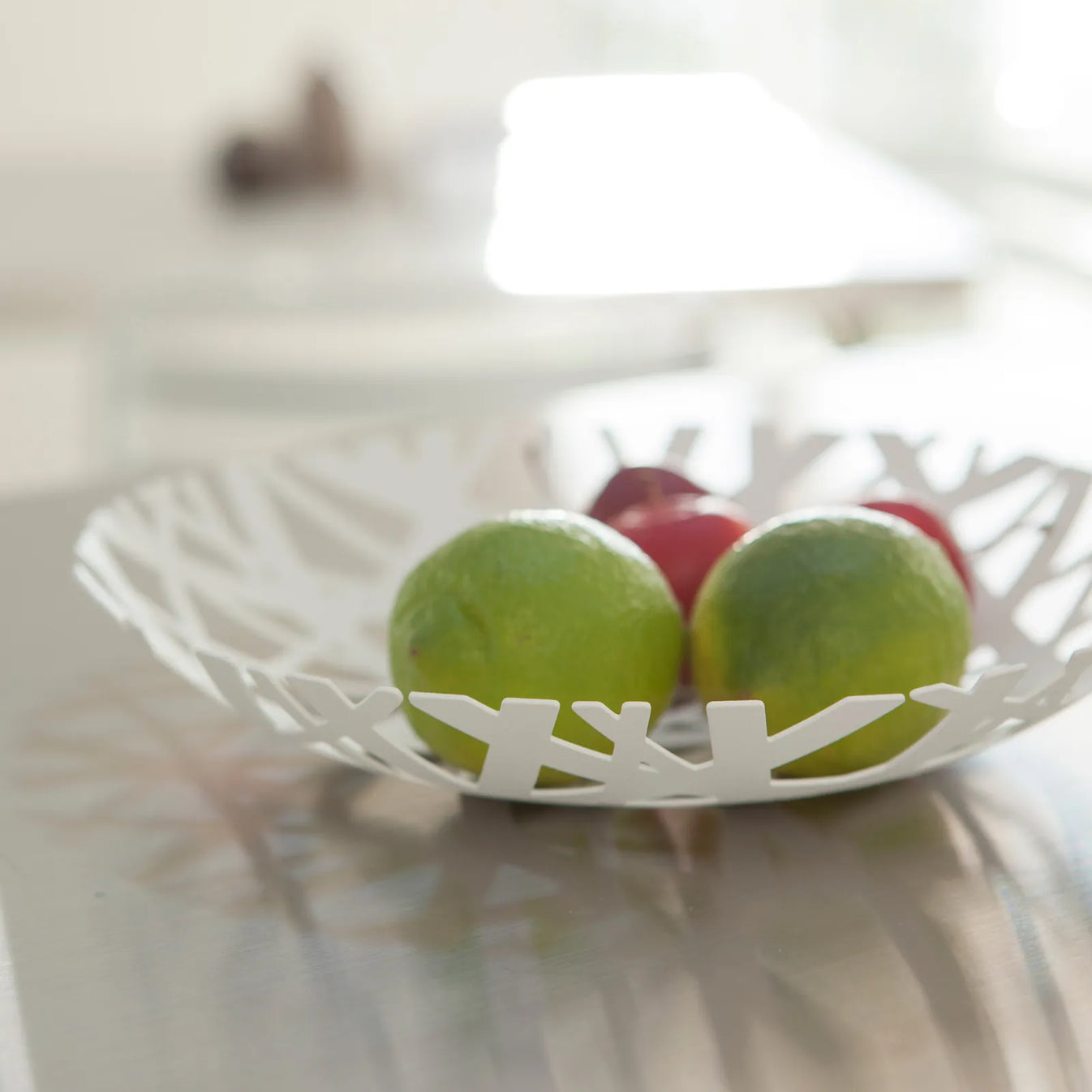 Detailaufnahme des weissen Obstkorbes mit Nestdesign aus Metall mit Limetten und roten Äpfeln.