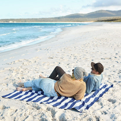 Blau-weiss gestreiftes Picknicktuch am Strand, auf dem zwei Personen sitzen und entspannen