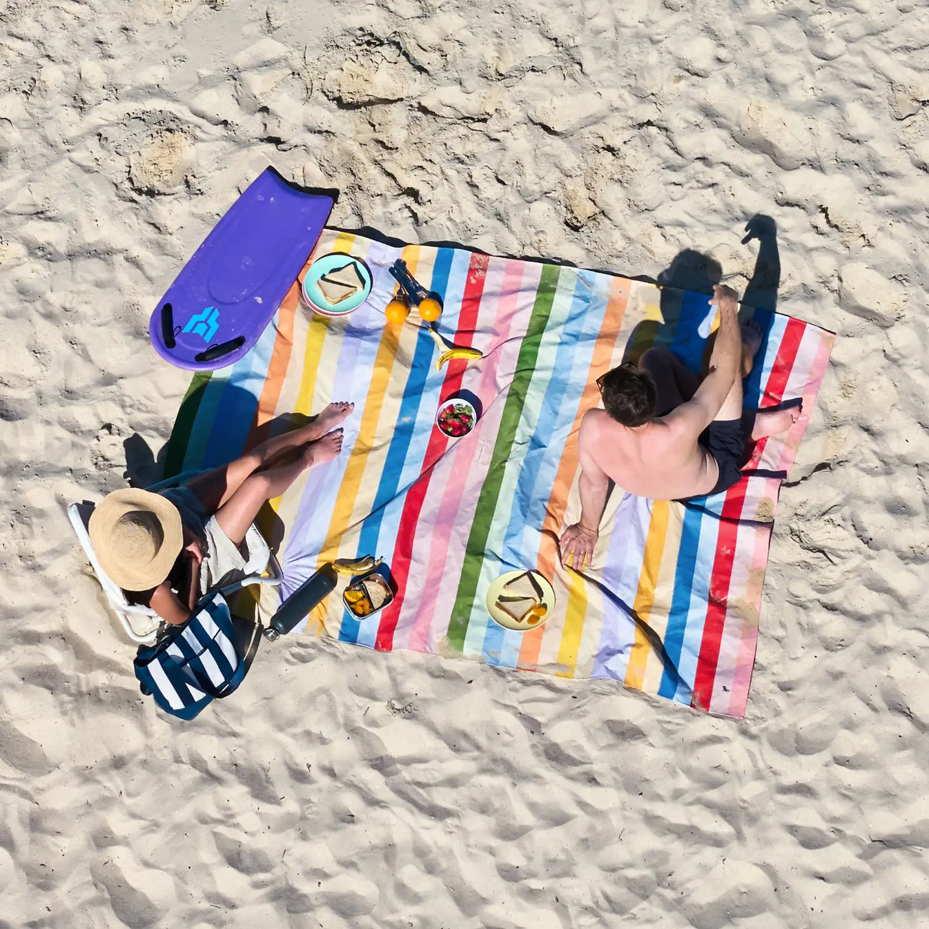 Gestreiftes Picknicktuch von oben mit zwei Personen, Essen und Strandutensilien auf Sand