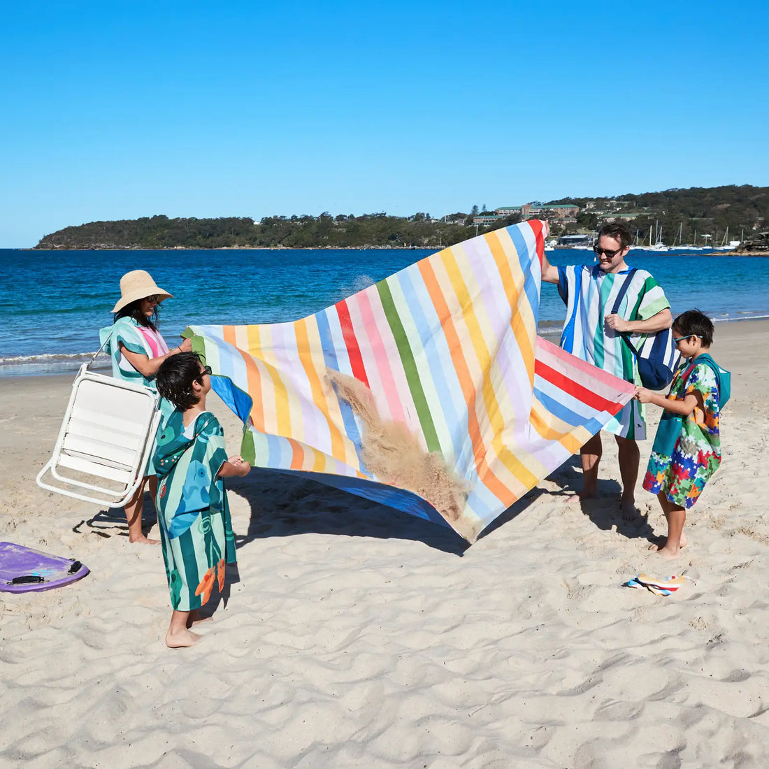 Grosses gestreiftes Picknicktuch wird am Strand ausgeschüttelt, während Sand herausfällt