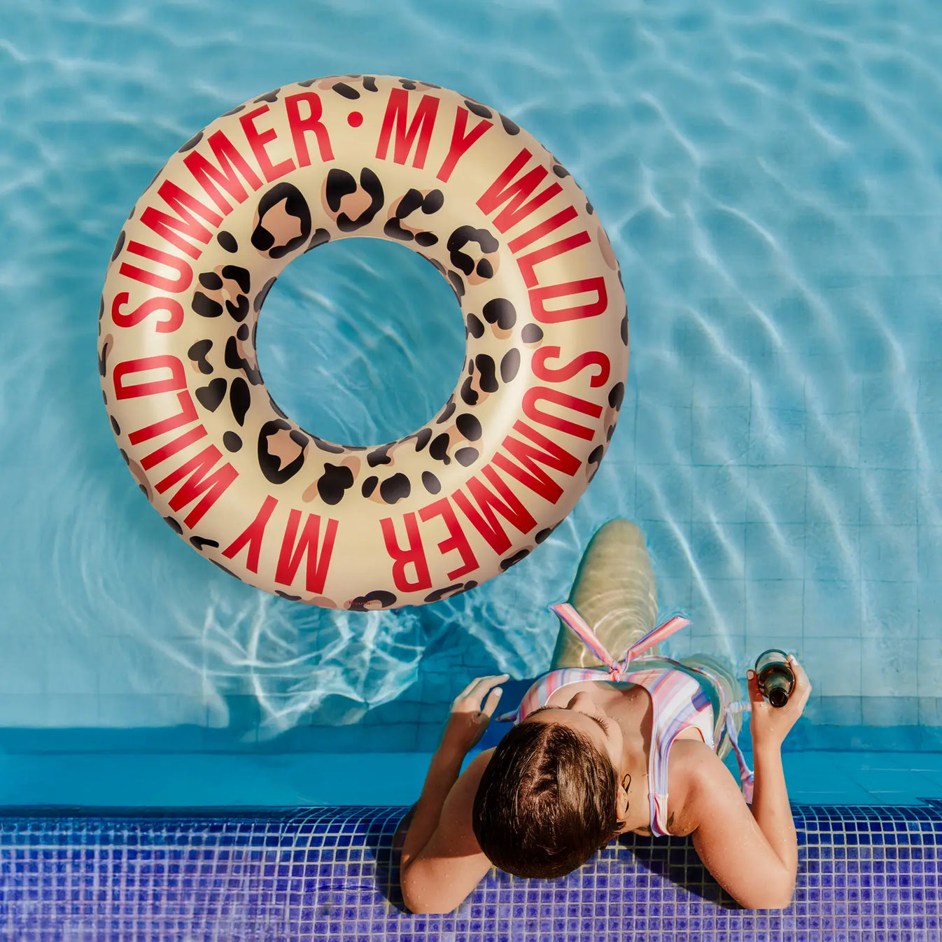 FISURA Schwimmring „My Wild Summer“ treibt im Pool neben einer Person am Beckenrand