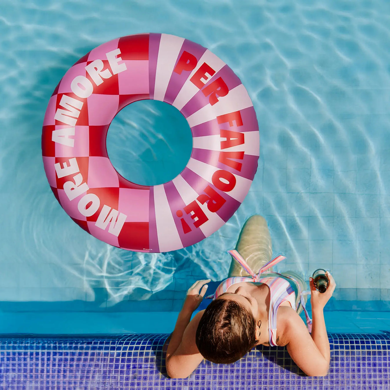 Rosa Schwimmring mit Schriftzug „More Amore Per Favore“ im Pool neben einer Person am Beckenrand