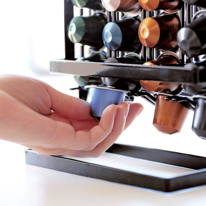 Detailansicht des Kaffeekapselhalters TOWER schwarz von YAMAZAKI bei der Entnahme einer Kaffeekapsel von unten, während die übrigen Kapseln automatisch nachrutschen.