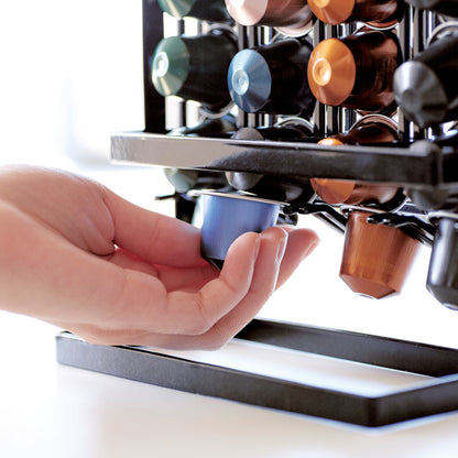 Detailansicht des Kaffeekapselhalters TOWER schwarz von YAMAZAKI bei der Entnahme einer Kaffeekapsel von unten, während die übrigen Kapseln automatisch nachrutschen.