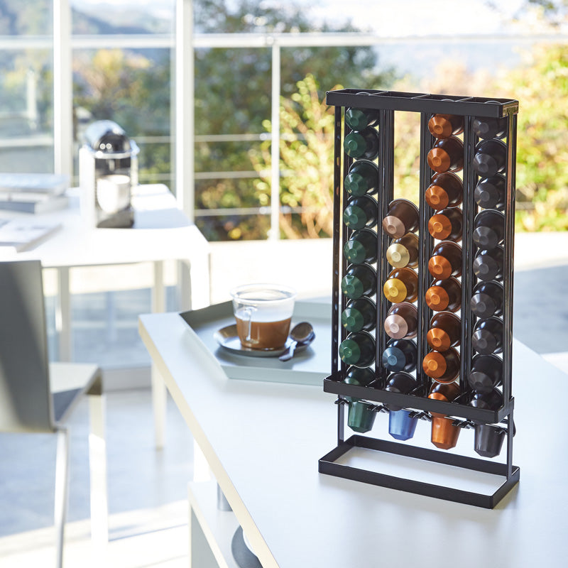 Kaffeekapselhalter TOWER schwarz von YAMAZAKI auf der Küchenzeile, befüllt mit Kaffeekapseln und griffbereit neben einer Tasse Kaffee.