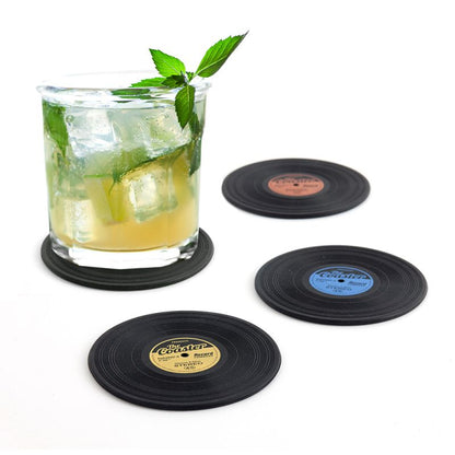 Ein Getränkeglas mit Eis und Minze steht auf einem schwarzen Untersetzer in Schallplatten-Optik. Drei weitere Untersetzer mit farbigen Mittenlabels liegen daneben.