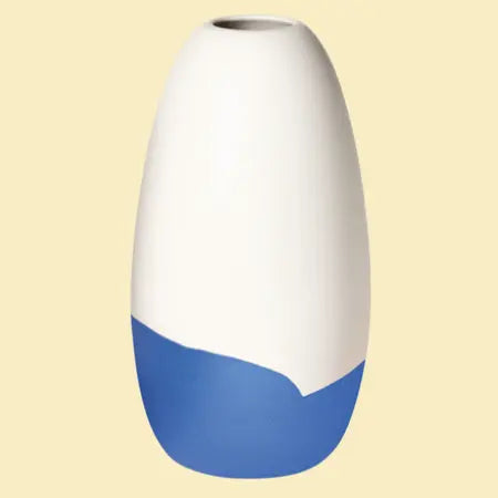 Konische Porzellanvase „Iapetus - dunkelblau“, seidenmatt weiss glasiert mit dunkelblauem Akzent am unteren Bereich, freigestellt vor hellglebem Hintergrund.