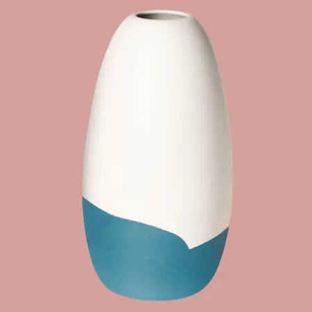 Konische Porzellanvase „Iapetus - petrol“, seidenmatt weiss glasiert mit petrol Akzent am unteren Bereich, freigestellt vor hellrotem Hintergrund.