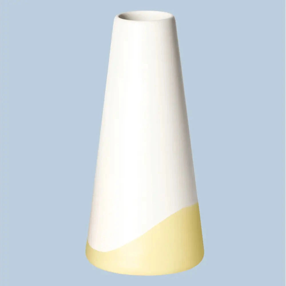 Schlanke, konische Porzellanvase „Neptun“ in seidenmattem Weiss mit gelbem Farbschwung am Fuss, freigestellt vor hellblauem Hintergrund.