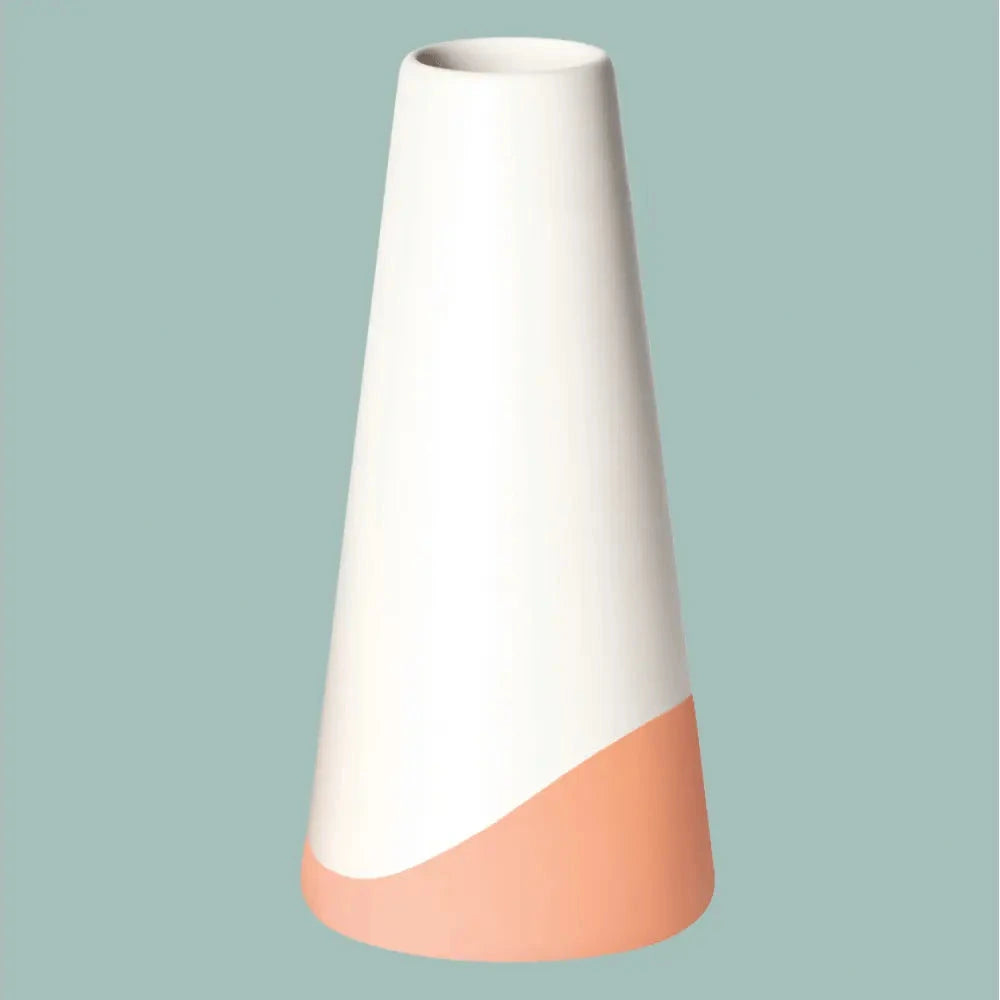 Porzellanvase „Neptun“ in Weiss mit warmem orangefarbenem Farbschwung am Fuss, freigestellt vor salbeigrünem Hintergrund.