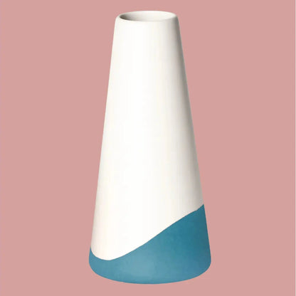 Konische Porzellanvase „Neptun“, seidenmatt weiss glasiert mit petrolfarbenem Akzent am unteren Bereich, freigestellt vor roséfarbenem Hintergrund.