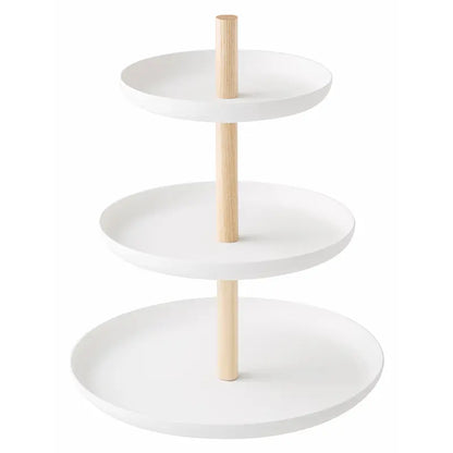 Dreistöckige weisse Etagère mit drei runden Schalen und hellen Holzstangen vor hellem Hintergrund. Sie eignet sich zum Servieren von Desserts und kleinen Leckereien.