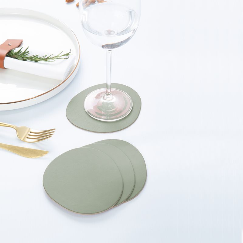 Ruca Stone Coasters sage green auf gedecktem Tisch: Untersetzer unter Weinglas, weitere Untersetzer gestapelt neben Teller und Besteck.