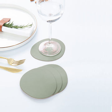 Ruca Stone Coasters sage green auf gedecktem Tisch: Untersetzer unter Weinglas, weitere Untersetzer gestapelt neben Teller und Besteck.