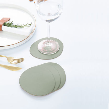 Ruca Stone Coasters sage green auf gedecktem Tisch: Untersetzer unter Weinglas, weitere Untersetzer gestapelt neben Teller und Besteck.
